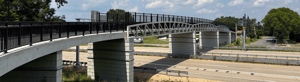 Pedestrian bridge crossing over a multi-lane highway on a sunny day.