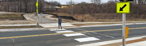 Pedestrian crossing a road at a marked crosswalk near a bike and pedestrian warning sign.