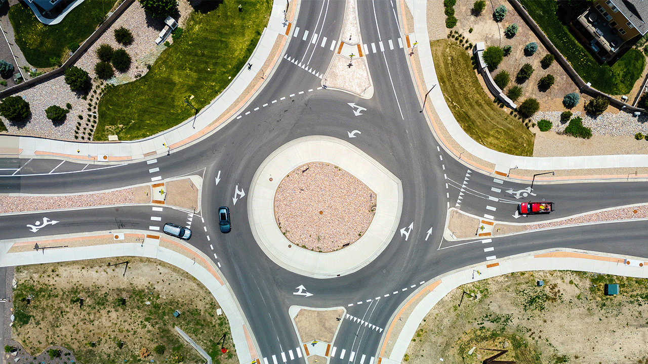 Aerial view of a landscaped roundabout with three cars and marked crosswalks.