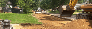 Excavator and road equipment grading a residential street during construction.
