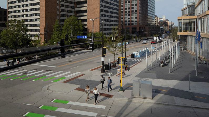 Downtown streetscape with pedestrians, protected bike crossings, and modern sidewalk improvements.