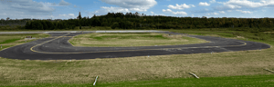 The turnaround loop at Longville Airport, shown as a paved circular taxiway surrounded by mowed grass and forest under a partly cloudy sky.