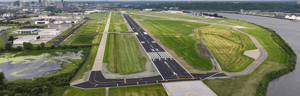 Aerial view of an airport runway labeled 14–32 surrounded by grassy fields and water.