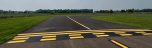 Freshly paved taxiway with bright yellow markings at a small airfield.