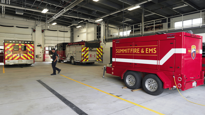 Image of the interior vehicle bay with multiple fire trucks and a man walking by.