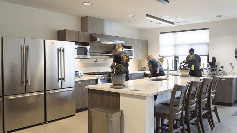 Three firefighters work in the station's new kitchen with stainless steel appliances and a central island.
