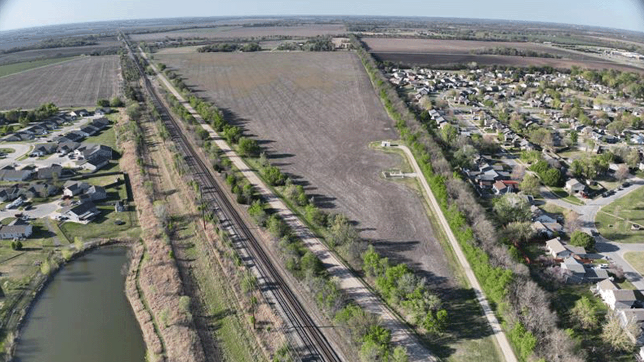 Aerial view of farmland bordered by a railroad, canal, and suburban neighborhoods.